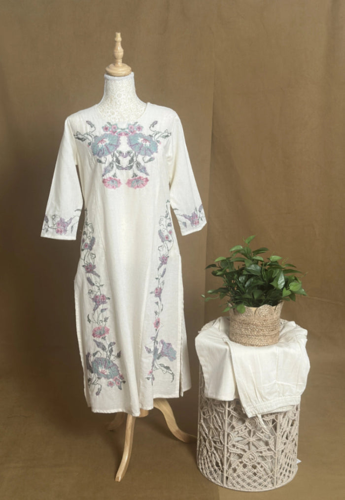 White embroidered dress on a mannequin with a plant on a small table against a brown background