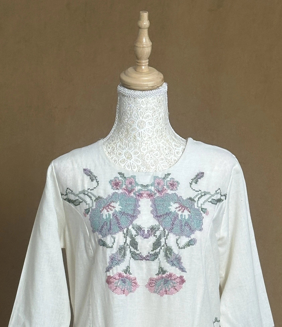 White blouse with floral embroidery on a mannequin against a brown background