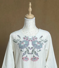 White blouse with floral embroidery on a mannequin against a brown background