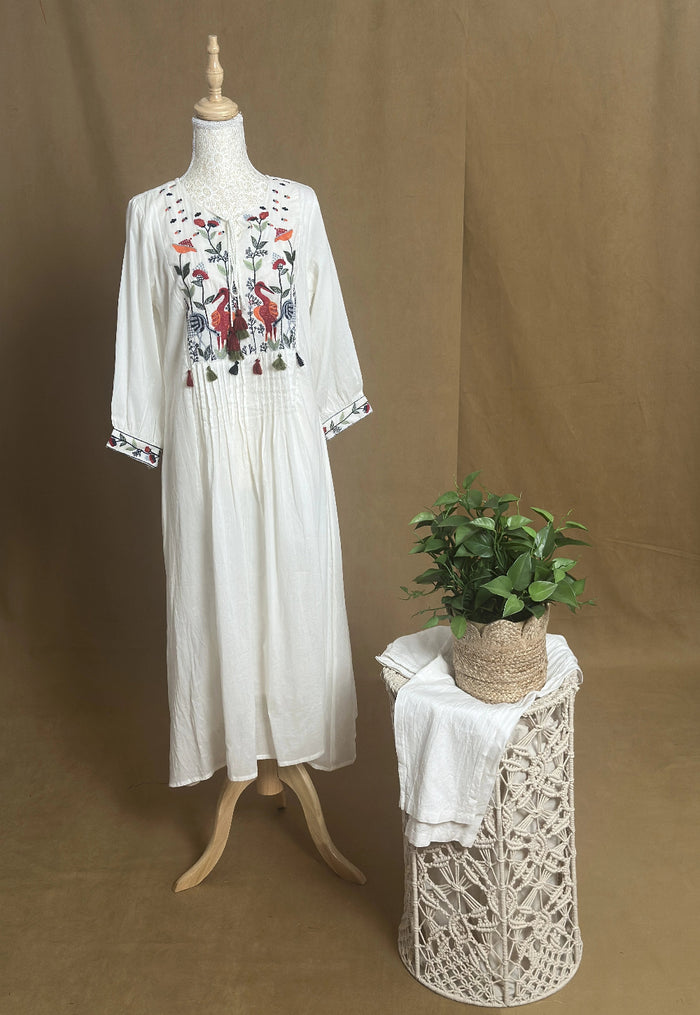 White embroidered dress on a mannequin with a small table and plant against a brown background