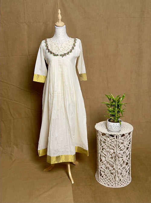 White dress with gold accents on a mannequin next to a small table with a plant against a brown background