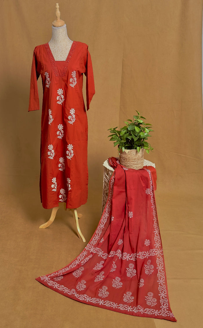 Rust orange dress with white floral patterns on a mannequin and draped over a chair against a brown background.