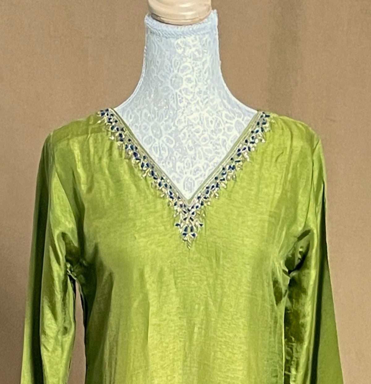 Green blouse with intricate beadwork on a mannequin against a brown background
