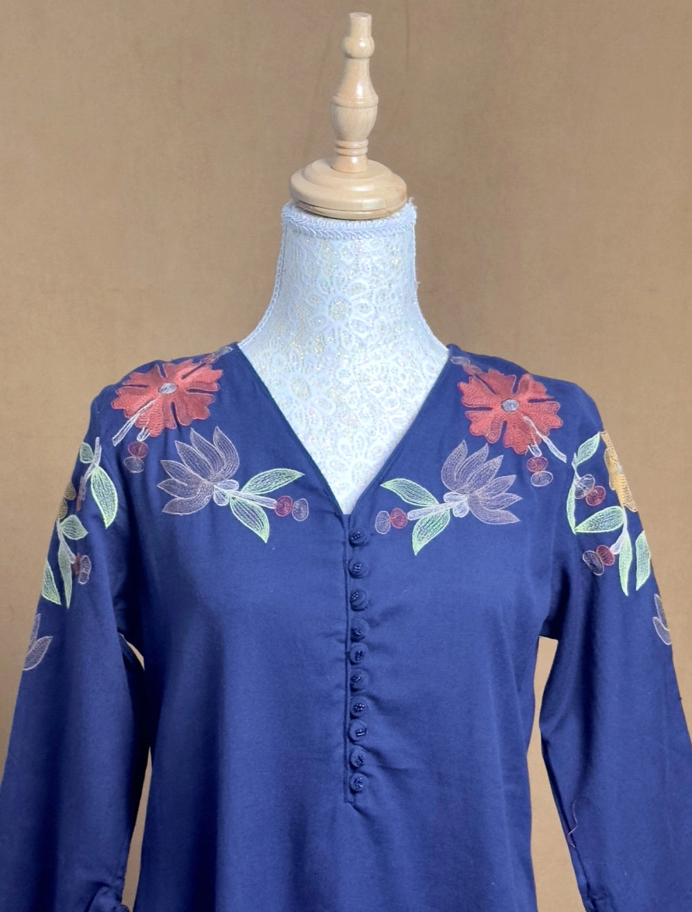 Blue blouse with floral embroidery on a mannequin against a beige background