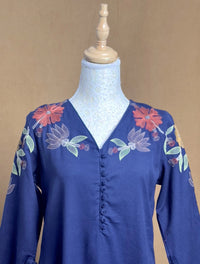 Blue blouse with floral embroidery on a mannequin against a beige background