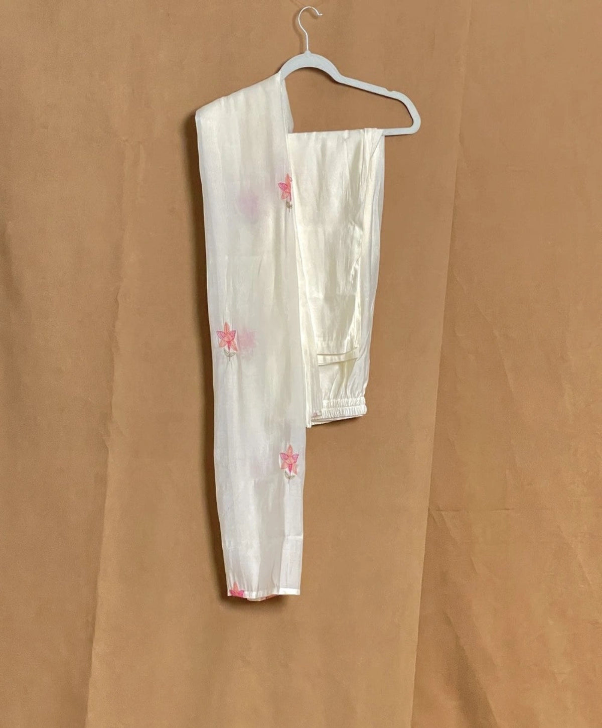 White outfit with floral patterns on a hanger against a brown background