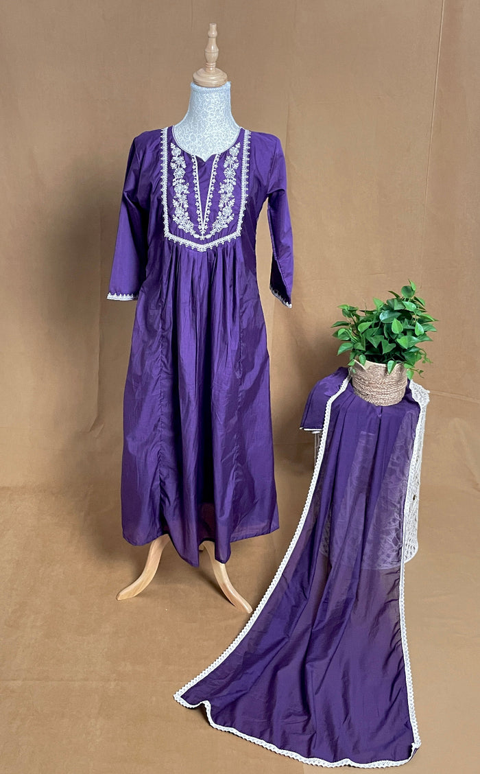 Purple dress with white embroidery on a mannequin and draped over a chair against a brown background.