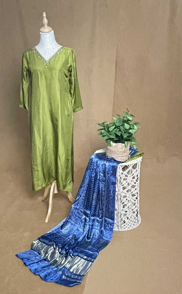 Green dress on a mannequin next to a blue fabric on a table with a plant against a brown background