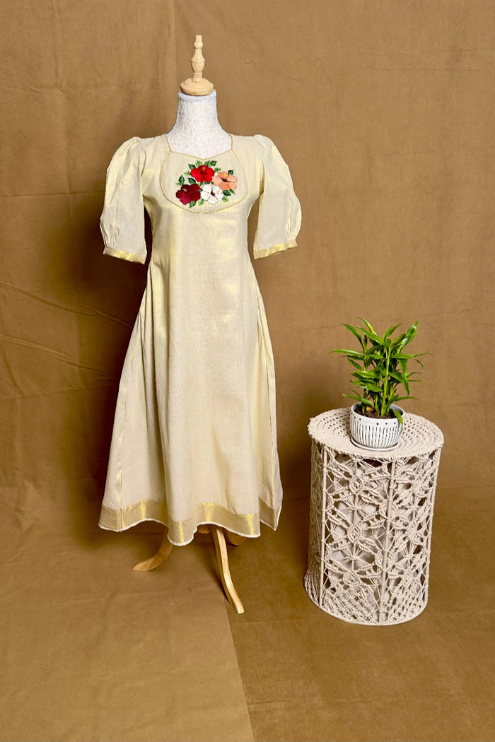 Vintage-style dress with floral embroidery on a mannequin next to a small table with a plant against a brown background