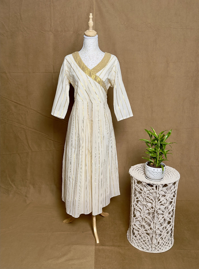 White dress on a mannequin next to a small table with a plant against a brown background