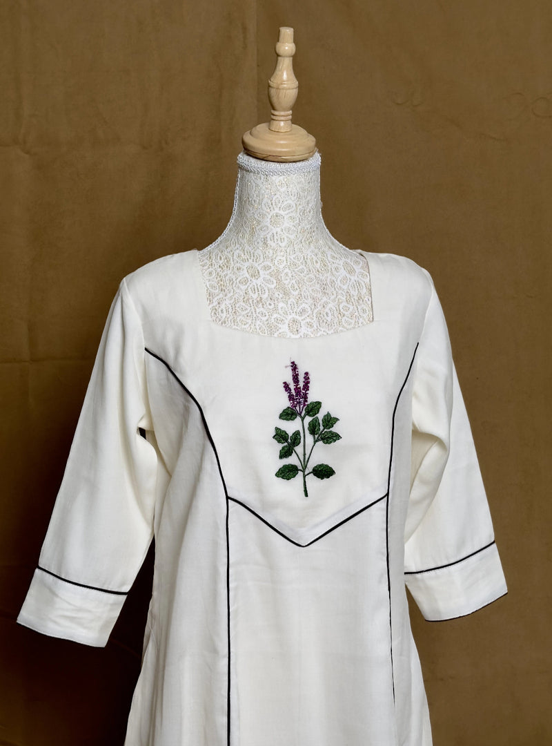 White dress with floral embroidery on a mannequin against a brown background