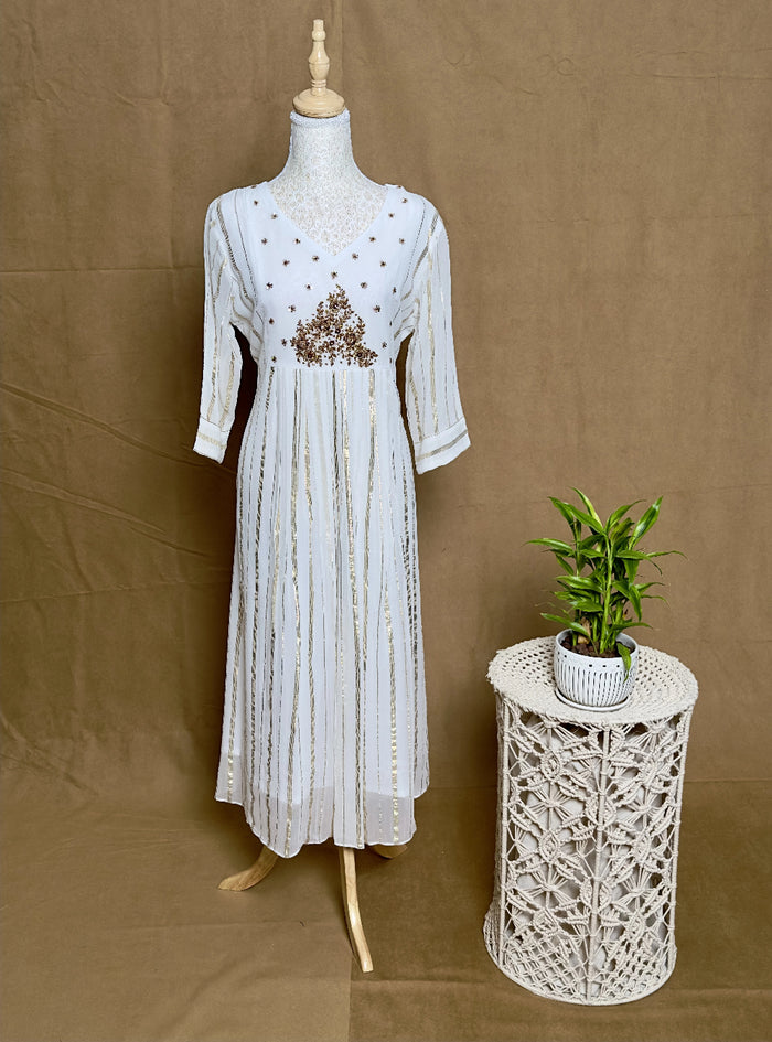 White dress on a mannequin next to a small table with a plant against a brown background