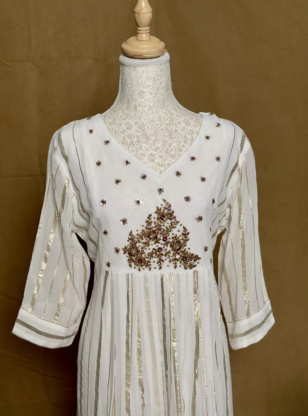 White dress with gold embroidery on a mannequin against a brown background