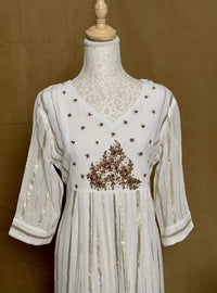 White dress with gold embroidery on a mannequin against a brown background