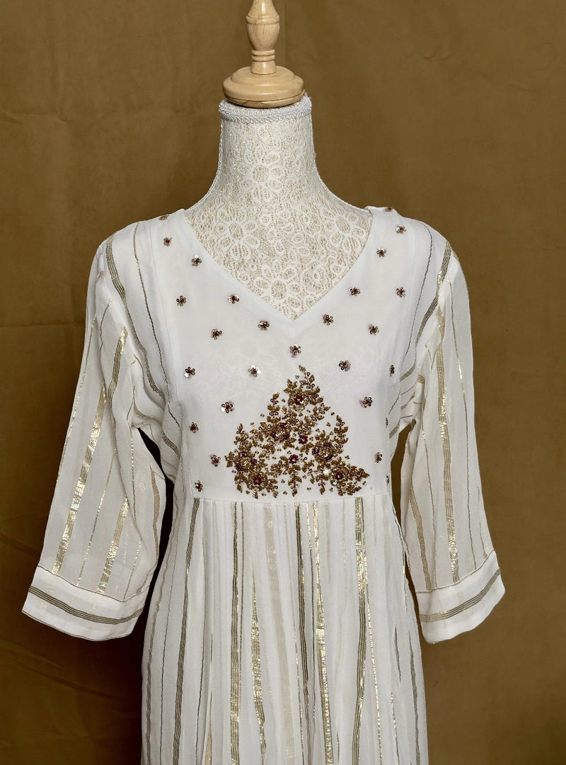 White dress with gold embroidery on a mannequin against a brown background