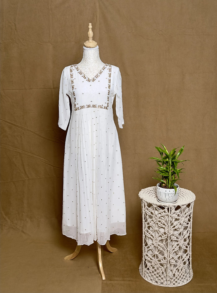 White dress on a mannequin next to a small plant on a woven stool against a brown background