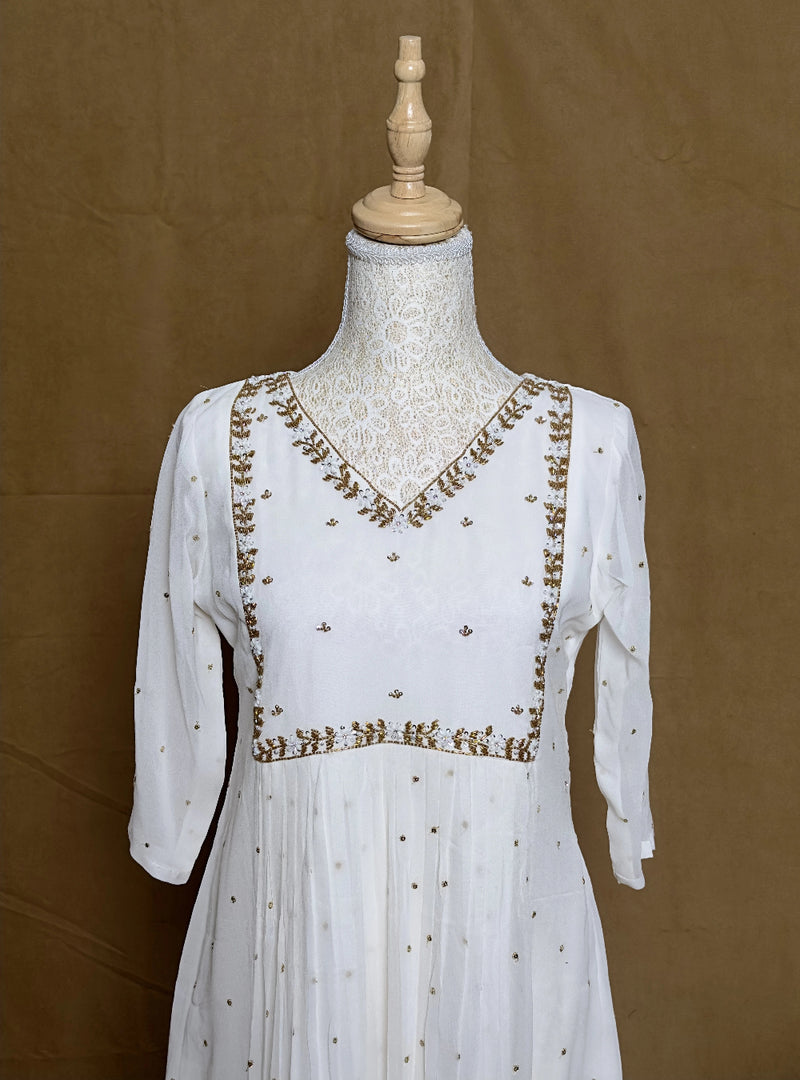 White dress with gold embroidery on a mannequin against a brown background