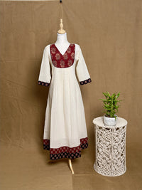 White dress with red and black patterns on a mannequin against a brown background