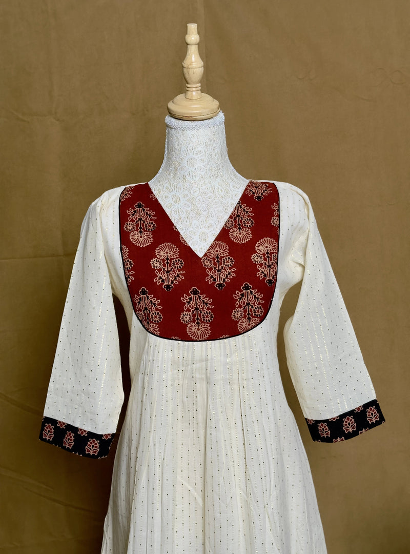 White dress with red and black embroidered top on a mannequin against a brown background